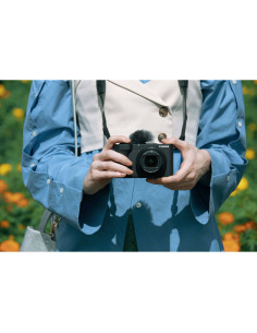 Femme portant une chemise bleue tient un appareil photo au mil, capture au Canon PowerShot V1 – Appareil photo compact 4K pou