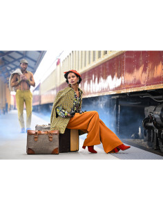 Femme au style vintage assise sur une valise à la gare, homme en arrière, capture au Nikon Z8 - Appareil Hybride Plein Format