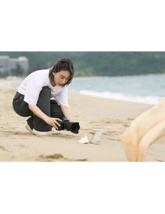 A woman crouching on the beach, focusing on a camera setup on the sand, captured with Nikon NIKKOR Z 24-70mm f/2.8 S II Lens A woman crouching on the beach, focusing on a camera setup on the sand, captured with Nikon NIKKOR Z 24-70mm f/2.8 S II Lens