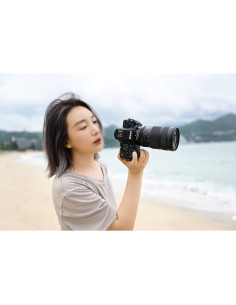 A person with short, dark hair stands on a beach, holding a camera with, captured with Nikon NIKKOR Z 24-70mm f/2.8 S II Lens A person with short, dark hair stands on a beach, holding a camera with, captured with Nikon NIKKOR Z 24-70mm f/2.8 S II Lens