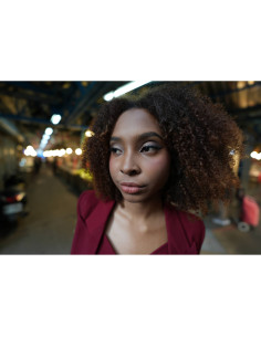 A woman with curly hair stands in a softly lit urban environment, captured with Sony FE 16mm f/1.8 G A woman with curly hair stands in a softly lit urban environment, captured with Sony FE 16mm f/1.8 G