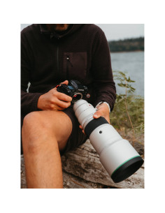 A person sitting by a river holding a camera with a long lens, casual outd, captured with Fujifilm XF 500mm f/5.6 R LM OIS WR A person sitting by a river holding a camera with a long lens, casual outd, captured with Fujifilm XF 500mm f/5.6 R LM OIS WR