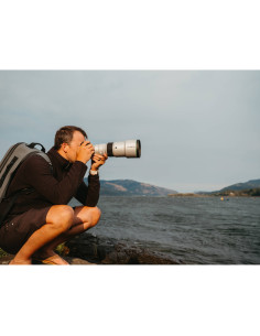 A man crouching by a river with a camera, wearing a backpack and capturing, captured with Fujifilm XF 500mm f/5.6 R LM OIS WR A man crouching by a river with a camera, wearing a backpack and capturing, captured with Fujifilm XF 500mm f/5.6 R LM OIS WR