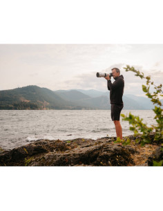 A man photographing near the shore, mountains in the background, soft even, captured with Fujifilm XF 500mm f/5.6 R LM OIS WR A man photographing near the shore, mountains in the background, soft even, captured with Fujifilm XF 500mm f/5.6 R LM OIS WR