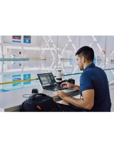 Un homme assis à une table, utilisant un ordinateur portable près d'une piscine, capture au Sony Alpha 1 II