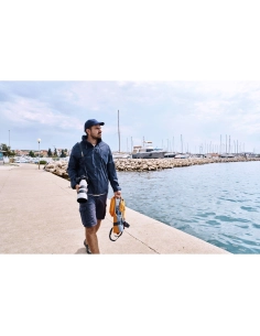 Un homme marche le long d'une jetée, appareil photo à la main, avec vue sur la mer et des bateaux, capture au Sony Alpha 1 II