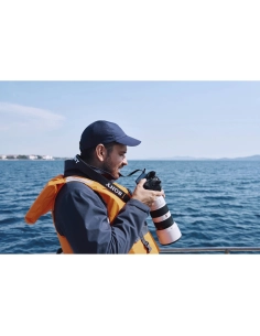 Homme avec un gilet de sauvetage prenant des photos près de l'eau sous un ciel dégagé, capture au Sony Alpha 1 II