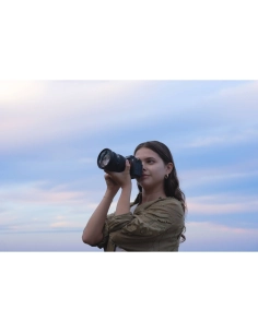 A young woman holding a camera against a softly colored sky at s, captured with Sony Alpha 7 V – Full Frame Mirrorless Camera A young woman holding a camera against a softly colored sky at s, captured with Sony Alpha 7 V – Full Frame Mirrorless Camera