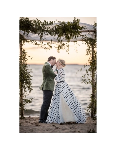 Pareja besándose en la playa al atardecer, envuelta en una decoración natural, capturado con Canon RF 135mm f/1.8 L IS USM