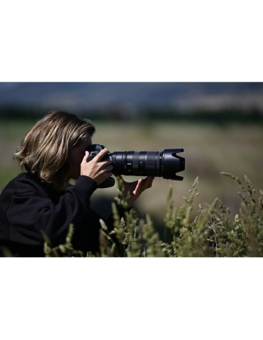 A woman photographing in a lush, green landscape, focusing intently on her subj, captured with Nikon Z 70-200mm f/2.8 VR S II