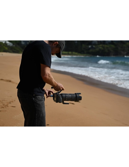 Hombre ajustando un equipo fotográfico en la playa con olas suaves al fo, capturado con Nikon NIKKOR Z 70-200mm f/2.8 VR S II