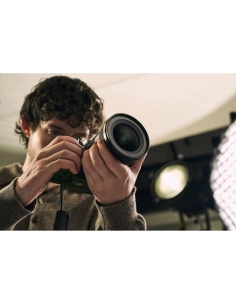 Joven con cabello rizado sosteniendo una cámara y ajustando el lente en un estudio de fotografía, capturado con Sony a7R VI Joven con cabello rizado sosteniendo una cámara y ajustando el lente en un estudio de fotografía, capturado con Sony a7R VI