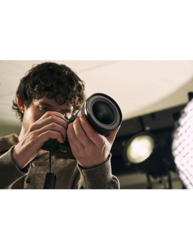 Joven con cabello rizado sosteniendo una cámara y ajustando el lente en un estudio de fotografía, capturado con Sony a7R VI