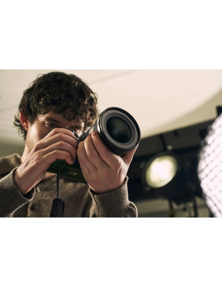 Joven con cabello rizado sosteniendo una cámara y ajustando el lente en un estudio de fotografía, capturado con Sony a7R VI