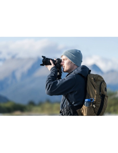 Un hombre con mochila y gorro gris fotografía un paisaje montañoso, capturado con Sony a7R VI