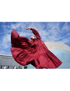 Una mujer en un vestido rojo gira en un entorno urbano bajo un cielo despejado, capturado con Sony a7R VI Una mujer en un vestido rojo gira en un entorno urbano bajo un cielo despejado, capturado con Sony a7R VI