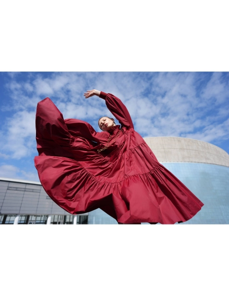 Una mujer en un vestido rojo gira en un entorno urbano bajo un cielo despejado, capturado con Sony a7R VI