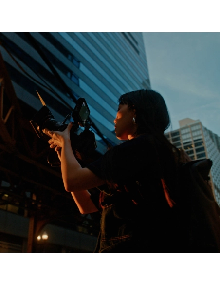 A woman holds a camera, capturing an urban sunset scene, captured with Canon EOS R6 V + RF 20-50mm f/4 L IS USM PZ