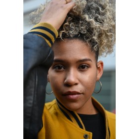A young woman with curly hair adjusts her hairstyle while wearing a yellow bomber jacket, captured with Nikon Z 28-75mm F2.8 A young woman with curly hair adjusts her hairstyle while wearing a yellow bomber jacket, captured with Nikon Z 28-75mm F2.8