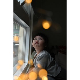 Un niño pequeño mirando por la ventana con expresión curiosa en una habitación iluminada, capturado con Nikon Z 28-75mm F2.8 Un niño pequeño mirando por la ventana con expresión curiosa en una habitación iluminada, capturado con Nikon Z 28-75mm F2.8