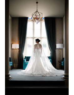 Une mariée en robe blanche avec un long voile devant une grande fenêtre, capture au Nikon Z 35mm f/1.2 S